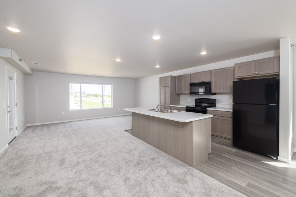 A spacious kitchen with a black refrigerator and a microwave above the counter.