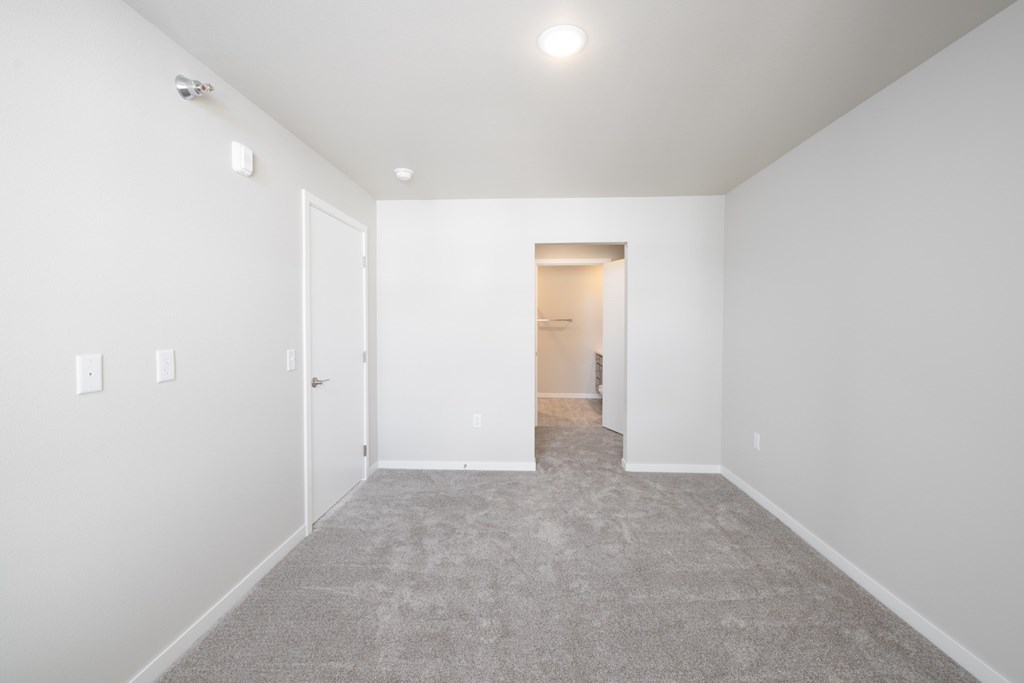 A white room with a carpeted floor and a doorway leading to another room.