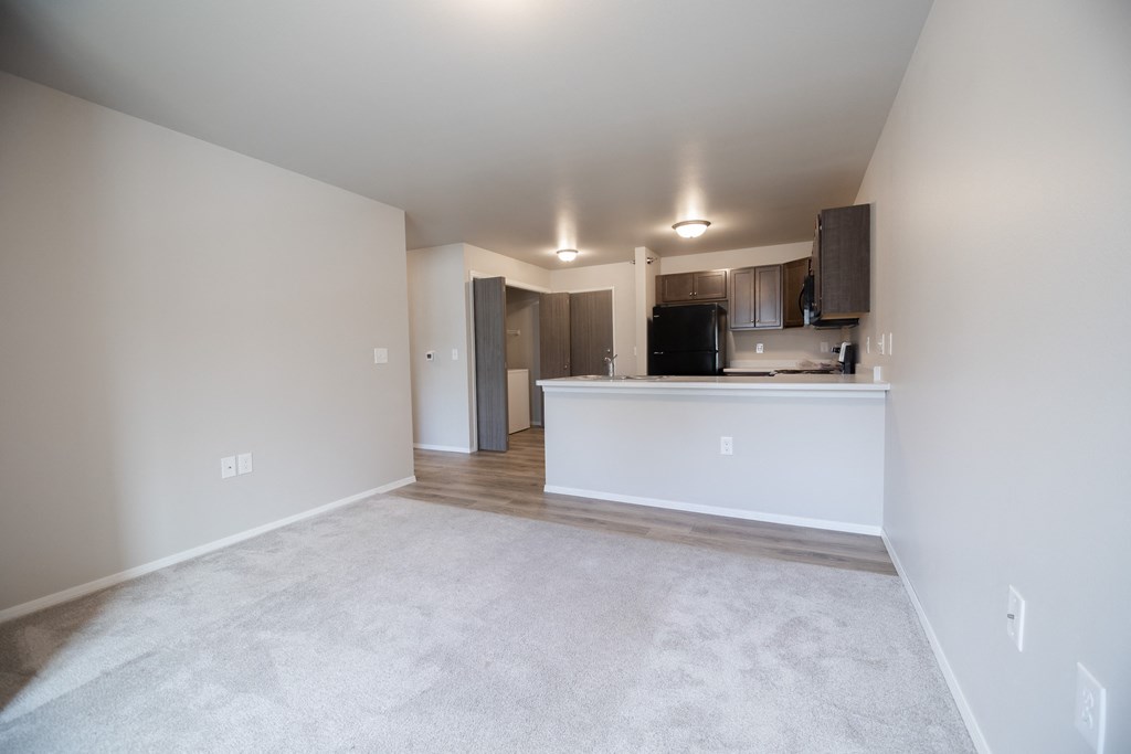 an empty living room with a kitchen in the corner
