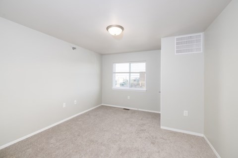 A spacious, empty room with a window and carpeted floor.