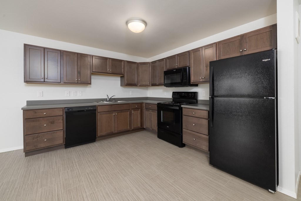 A black refrigerator is in a kitchen with brown cabinets.