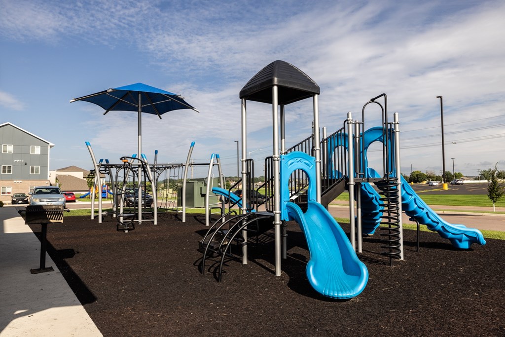 A playground with a blue slide and a black umbrella.