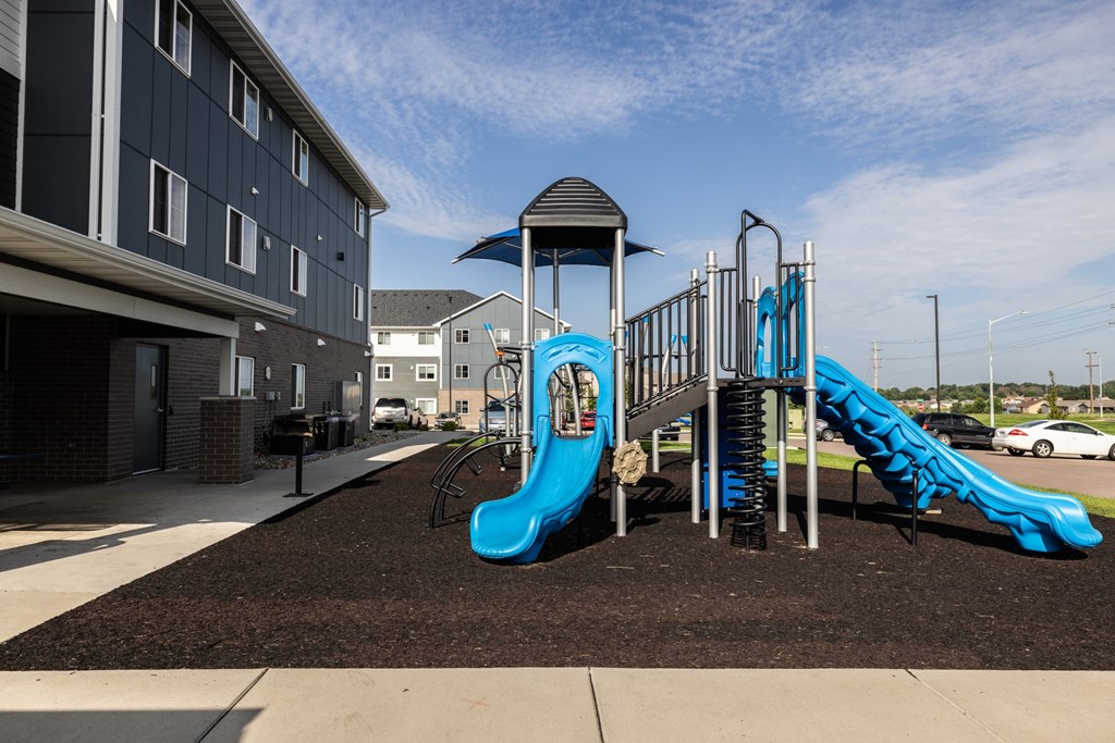 A playground with a blue slide and a black and white building in the background.