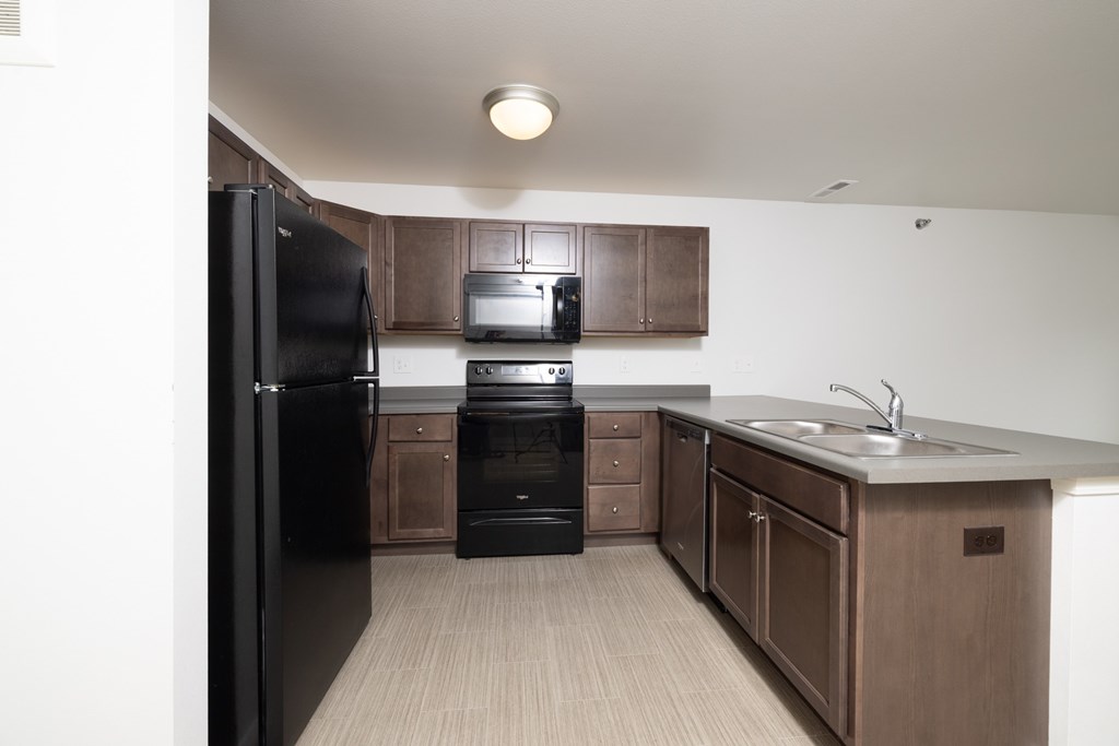 A black refrigerator is in a kitchen with brown cabinets.