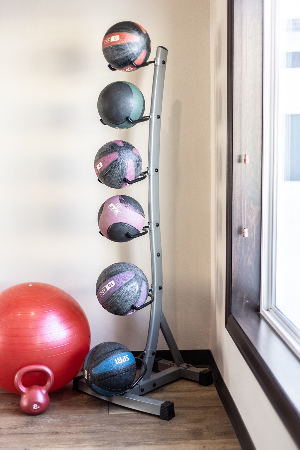 a rack of exercise balls in a workout room with a window