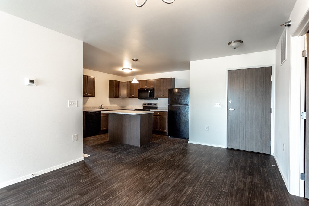 an empty apartment with a kitchen and a dark wood floor