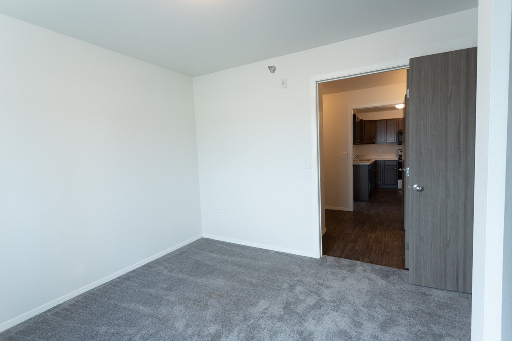 an empty living room with a door to a kitchen