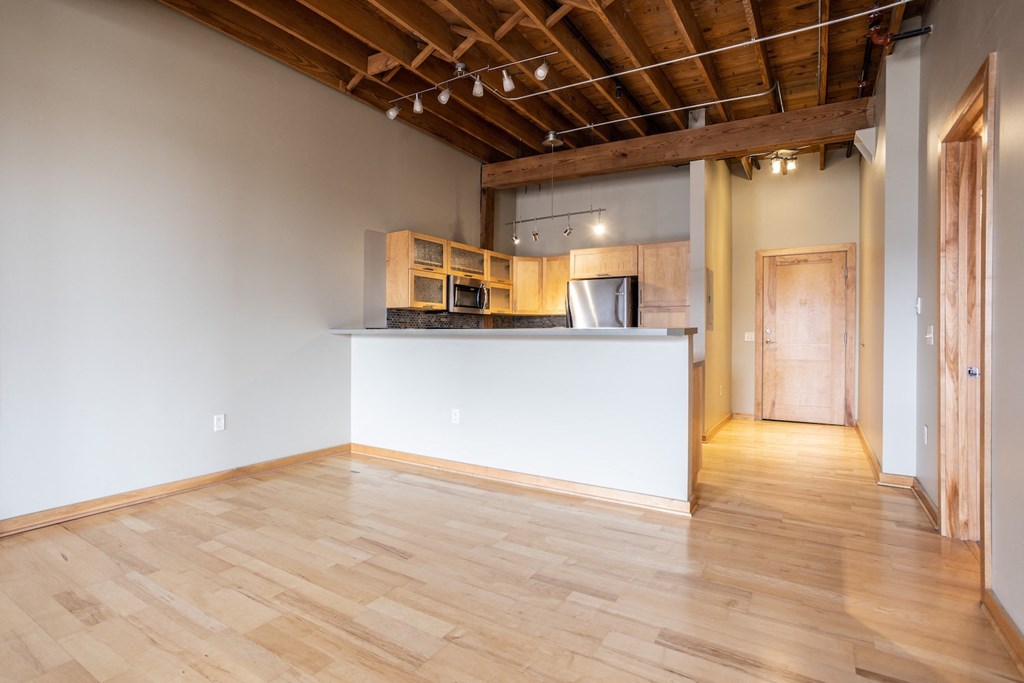 an empty living room with a kitchen and wood floors