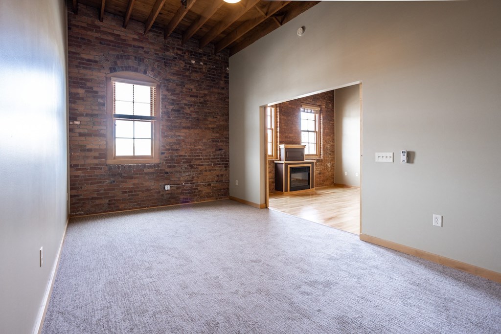 an empty living room with a brick wall and white carpet