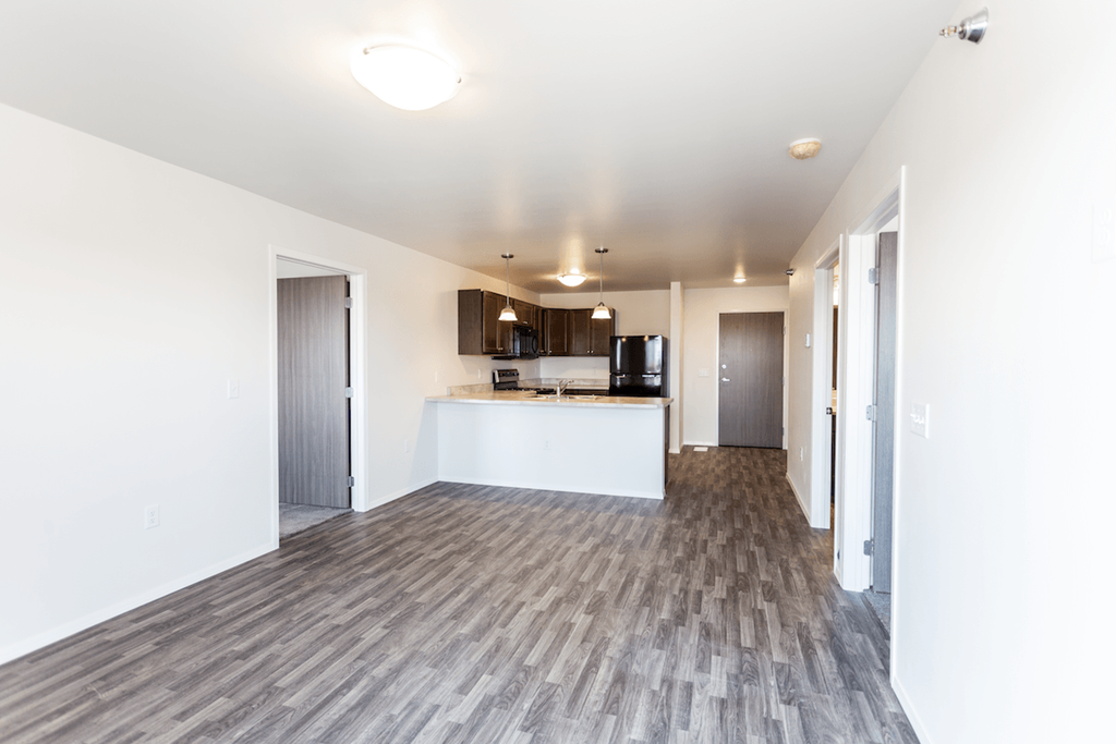 an empty apartment with white walls and wood flooring and a kitchen