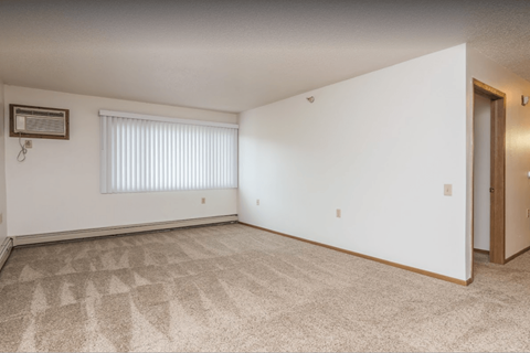 the living room and bedroom of an apartment with white walls and carpet
