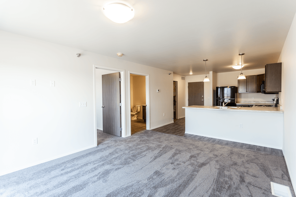 an empty living room with a kitchen and a door to a bedroom