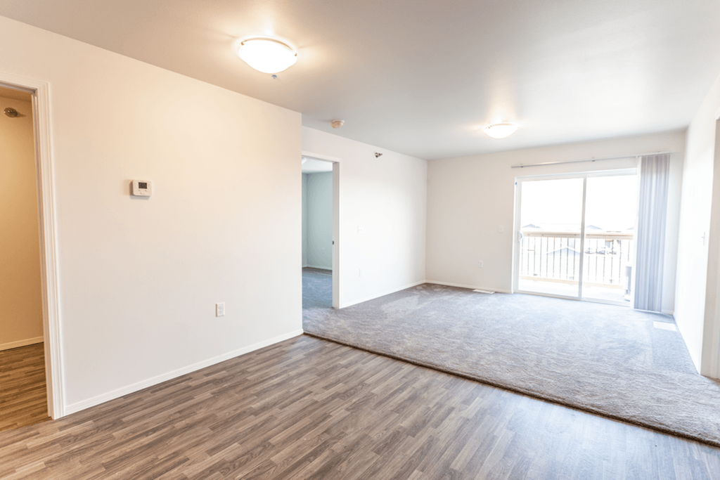 the living room and dining room of an apartment with wood flooring and white walls
