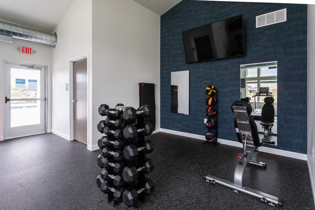 a gym with weights and a tv on the wall and a door