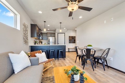 A modern living room with a grey couch, a wooden coffee table, and a dining table with chairs.