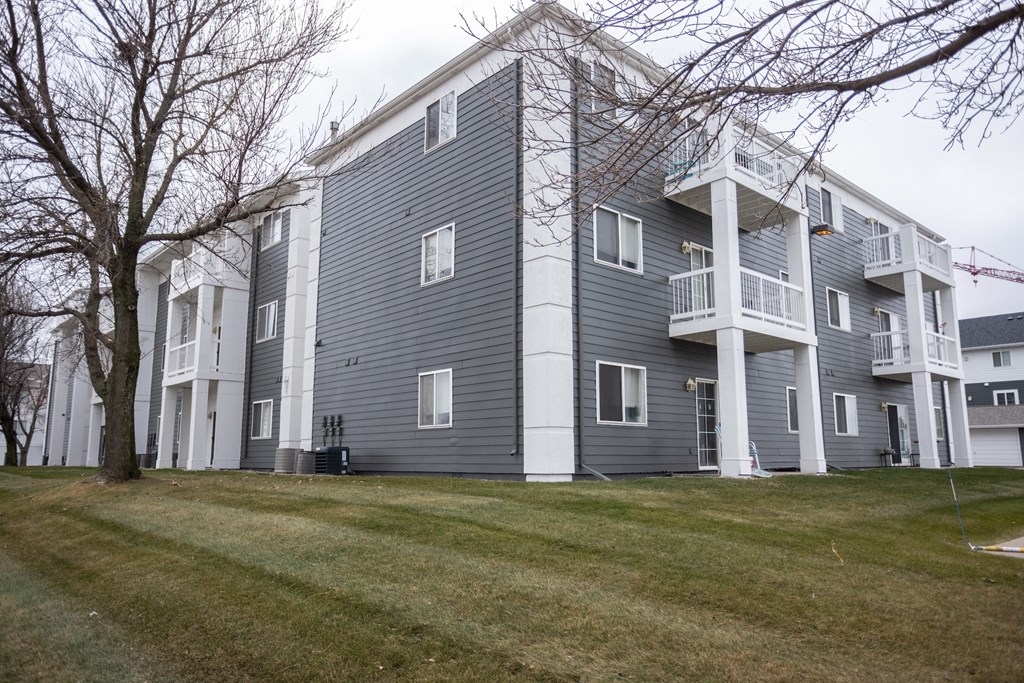 a gray apartment building with a yard in front of it