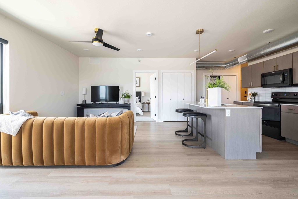 A modern living room with a brown sofa and a kitchen in the background.