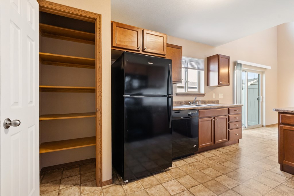 A black refrigerator is in a kitchen with wooden cabinets and a white door.