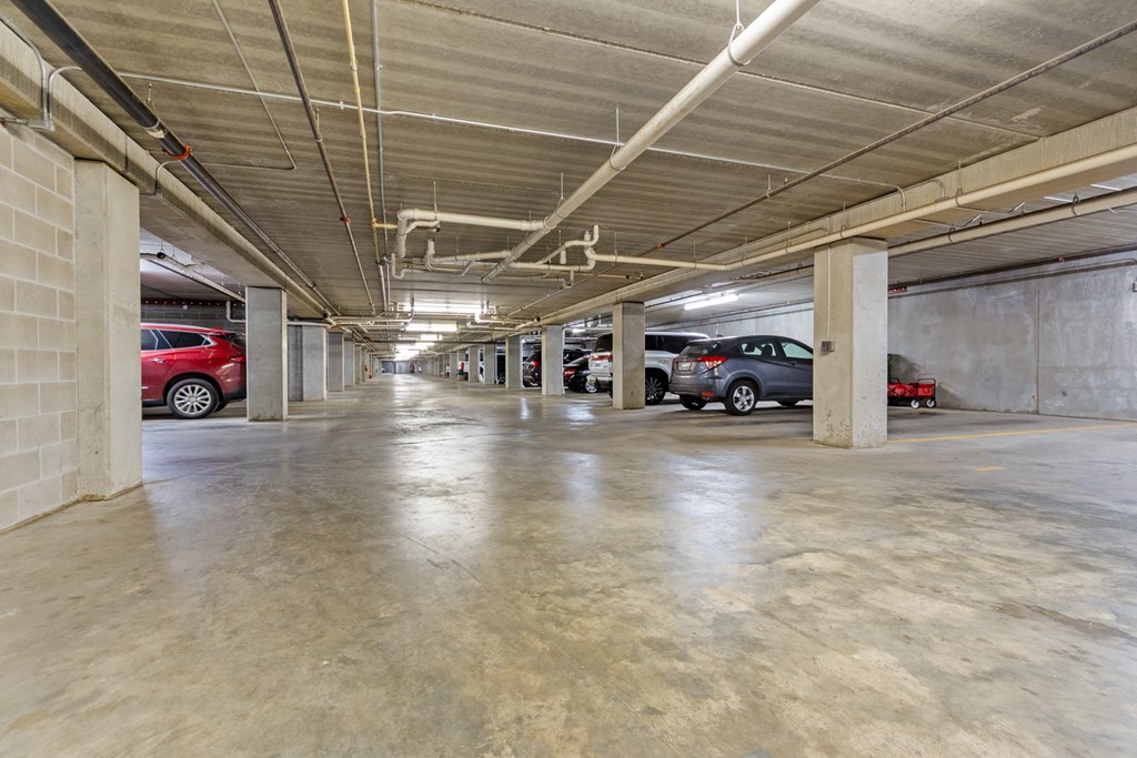 A parking garage with concrete floors and walls, and cars parked in the background.