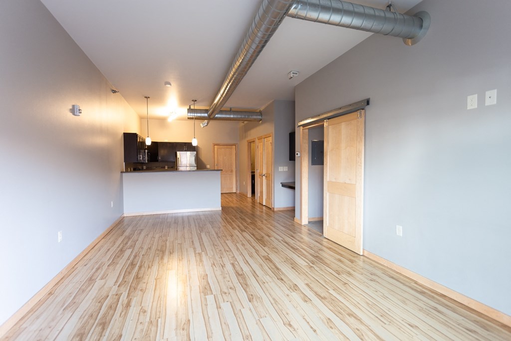an empty living room with wood floors and a kitchen