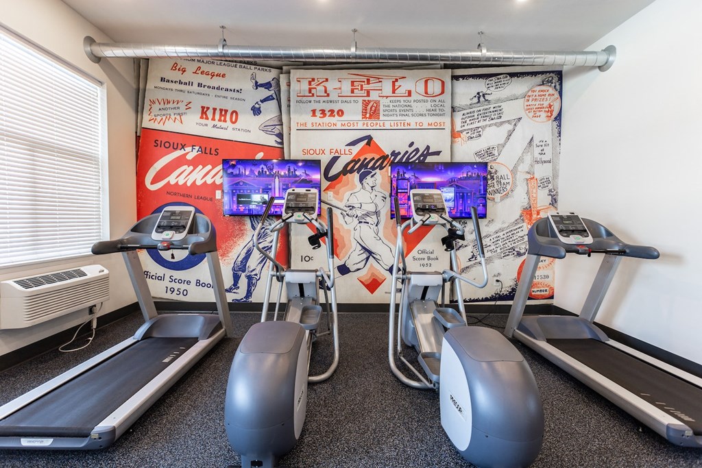 a gym with cardio machines and a wall of coke ads