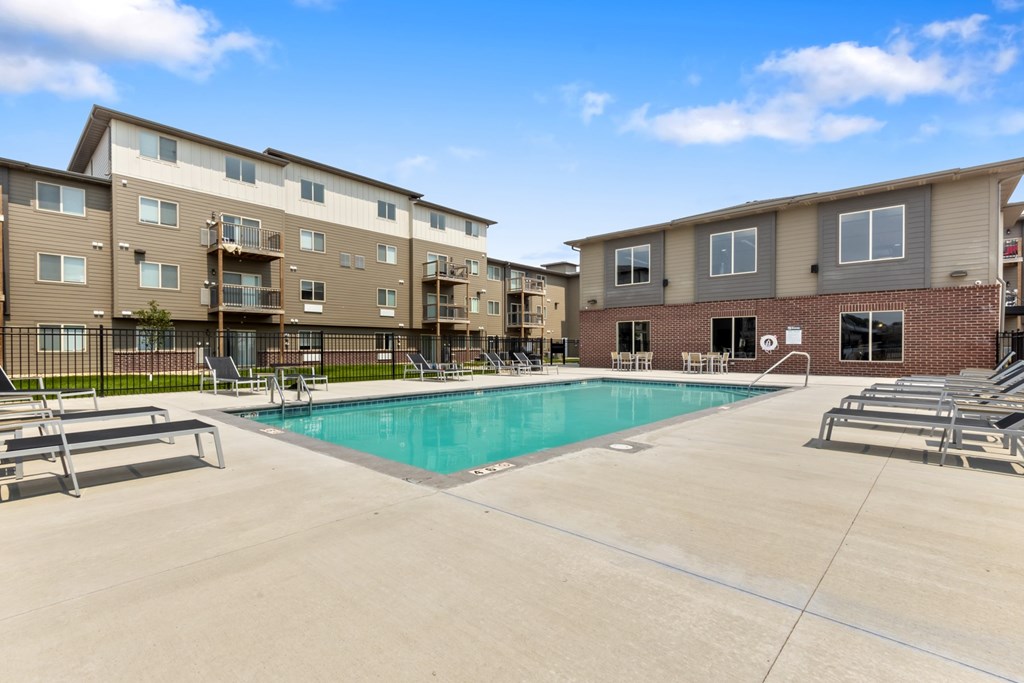 A swimming pool is surrounded by sun loungers in front of apartment buildings.