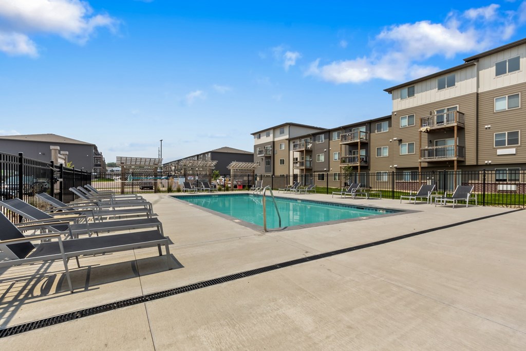 A swimming pool surrounded by sun loungers and apartment buildings.