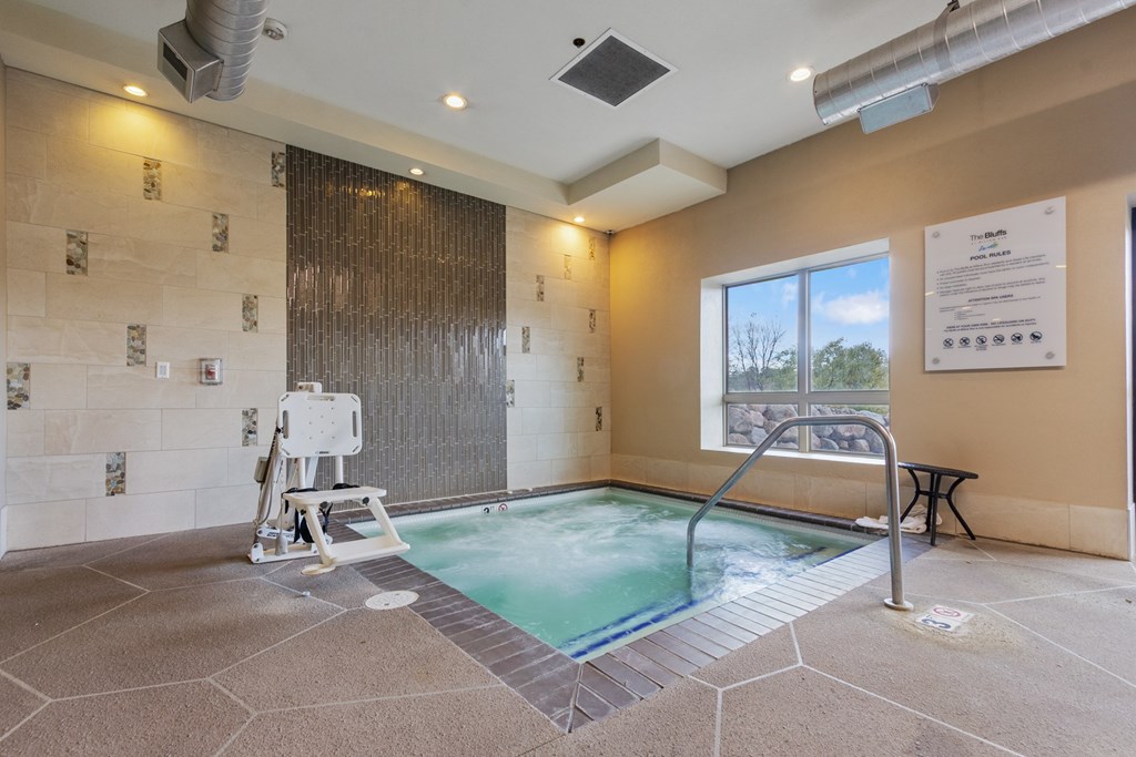 A hot tub in a room with a window and a wall of tiles.