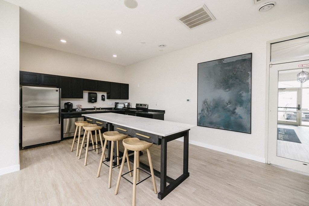 a kitchen with a long island with bar stools and a stainless steel refrigerator