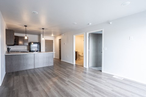 an empty living room with a kitchen and a door to a hallway