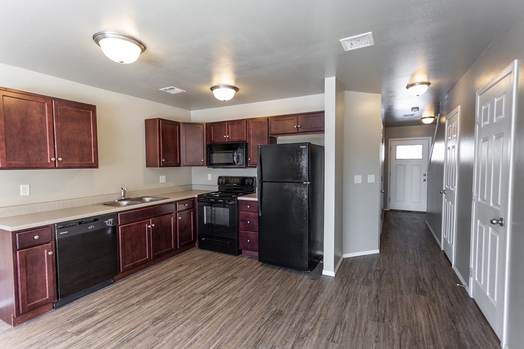 an empty kitchen with wood flooring and a black refrigerator