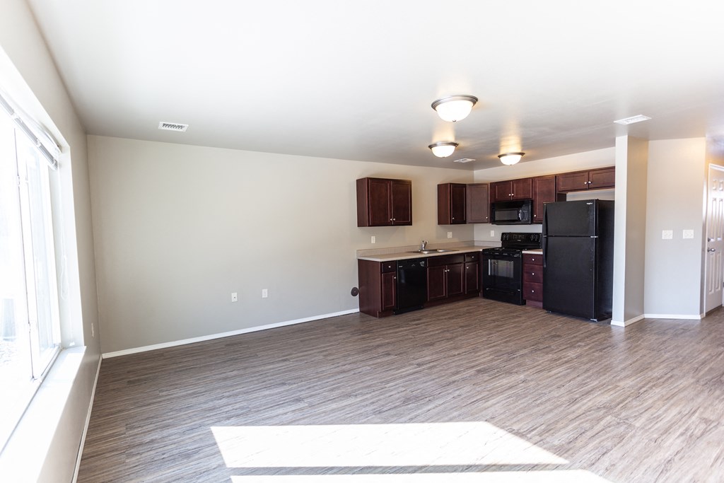 a kitchen and living room with a wood floor and a black refrigerator