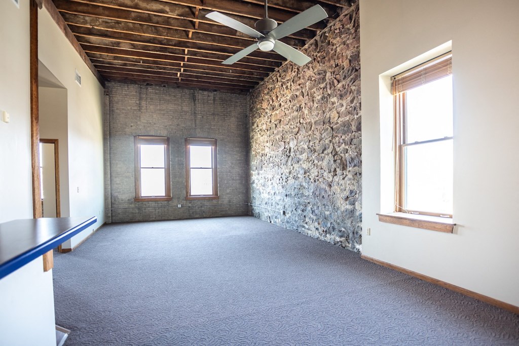 an empty room with a ceiling fan and a stone wall