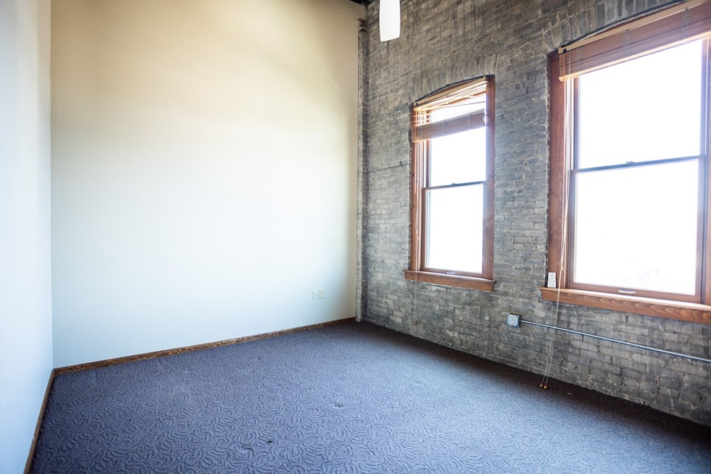 an empty room with two windows and a blue carpet