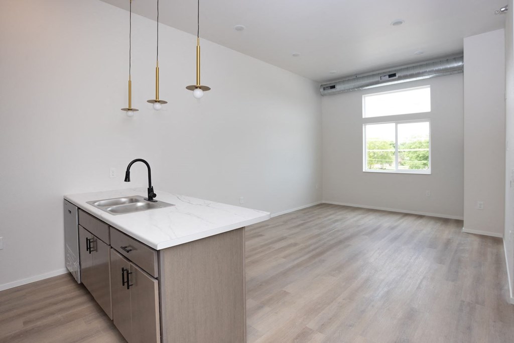 an empty living room with a kitchen and a window