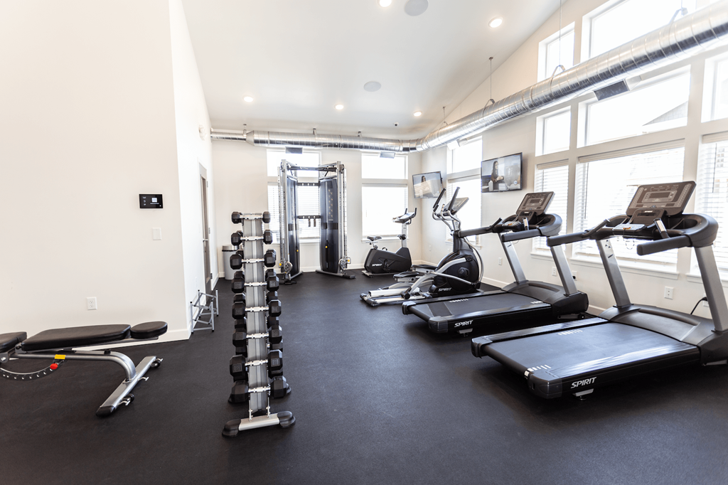 a gym with treadmills and other exercise equipment in a room with windows