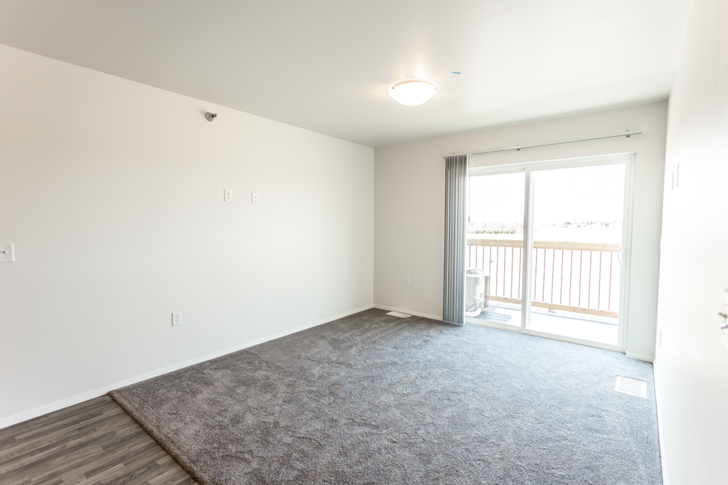 A room with a carpeted floor and a sliding glass door leading to a balcony.