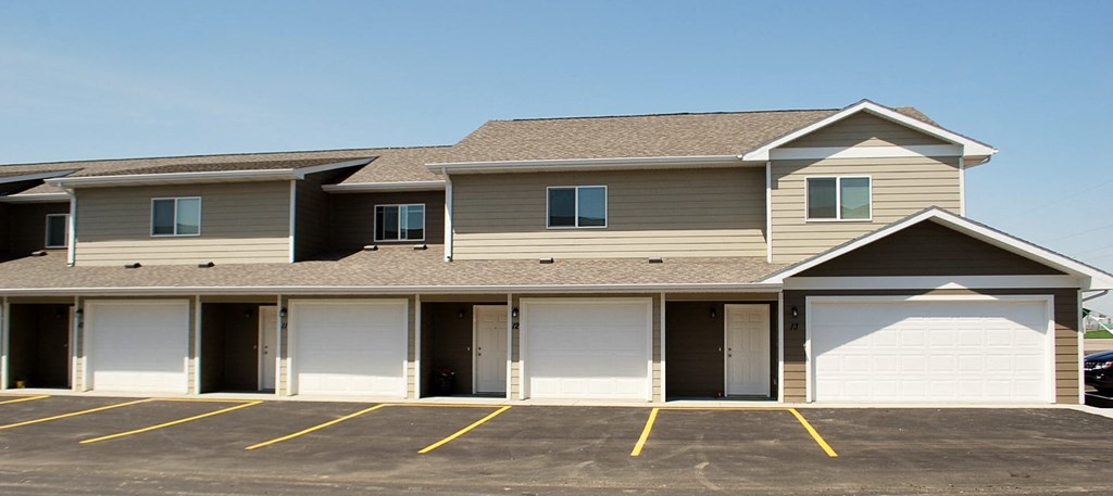a tan house with white garage doors in a parking lot