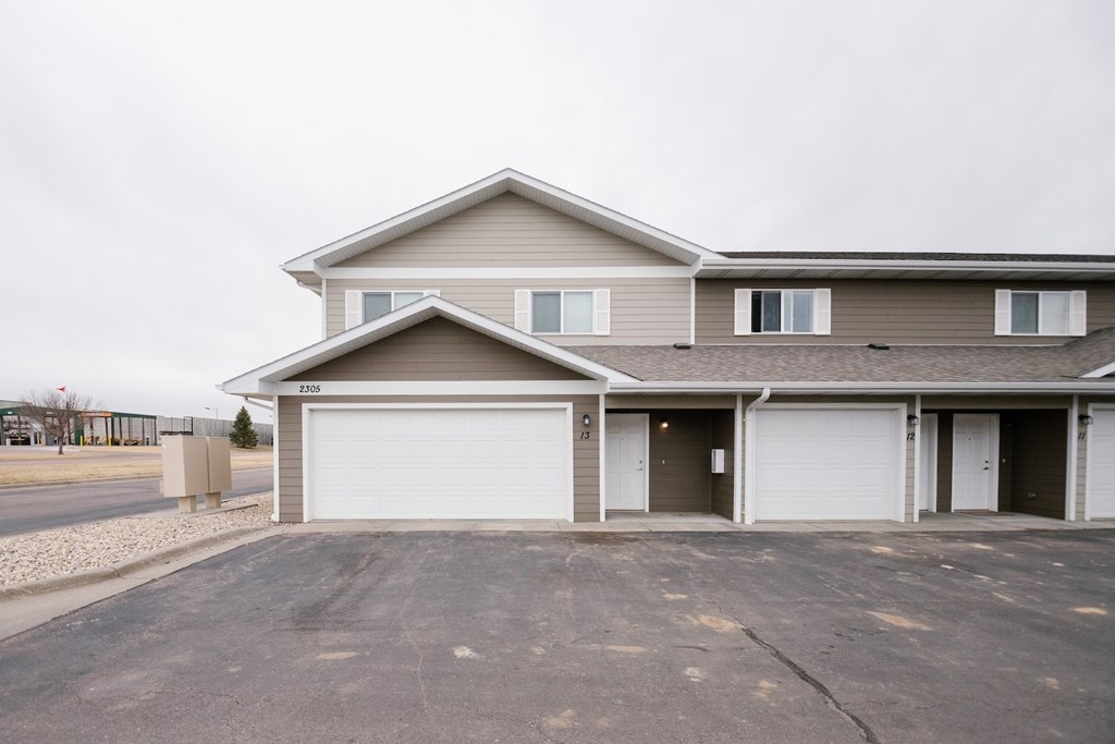 A two-story house with a garage is situated in a parking lot.