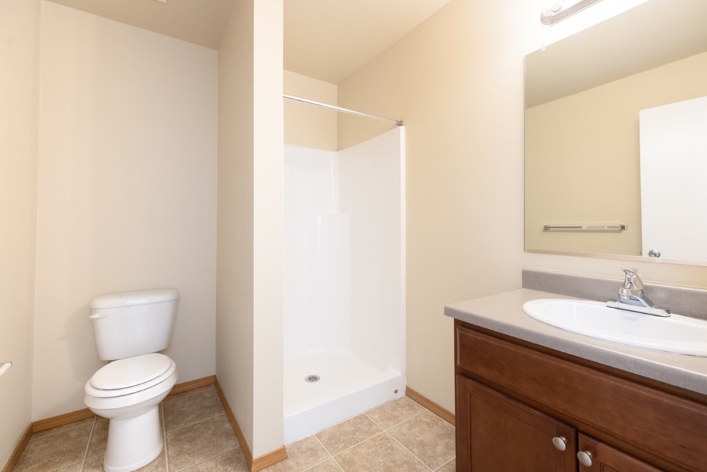 A white toilet is in a bathroom with a sink and mirror.