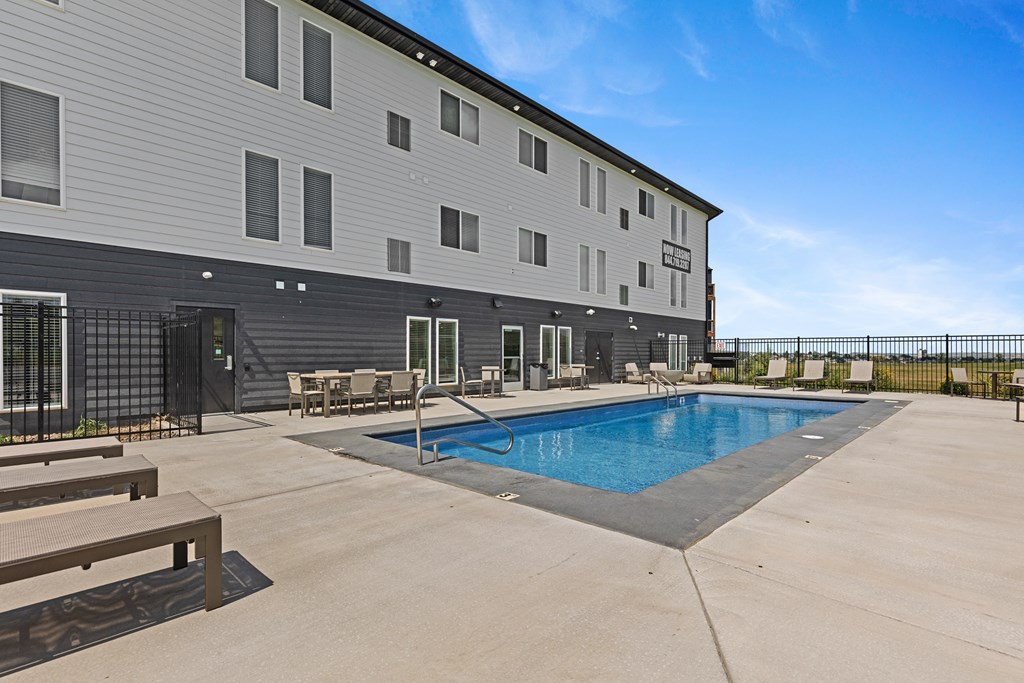 A large outdoor swimming pool is surrounded by a concrete patio and wooden benches.