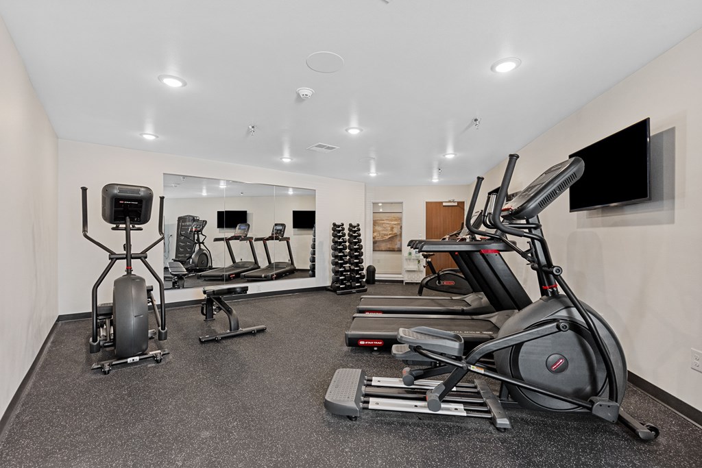 A spacious gym with a variety of equipment including treadmills, elliptical machines, and a television.