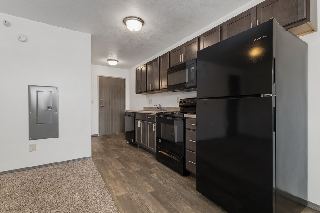 A black refrigerator in a kitchen with wooden floors and cabinets.