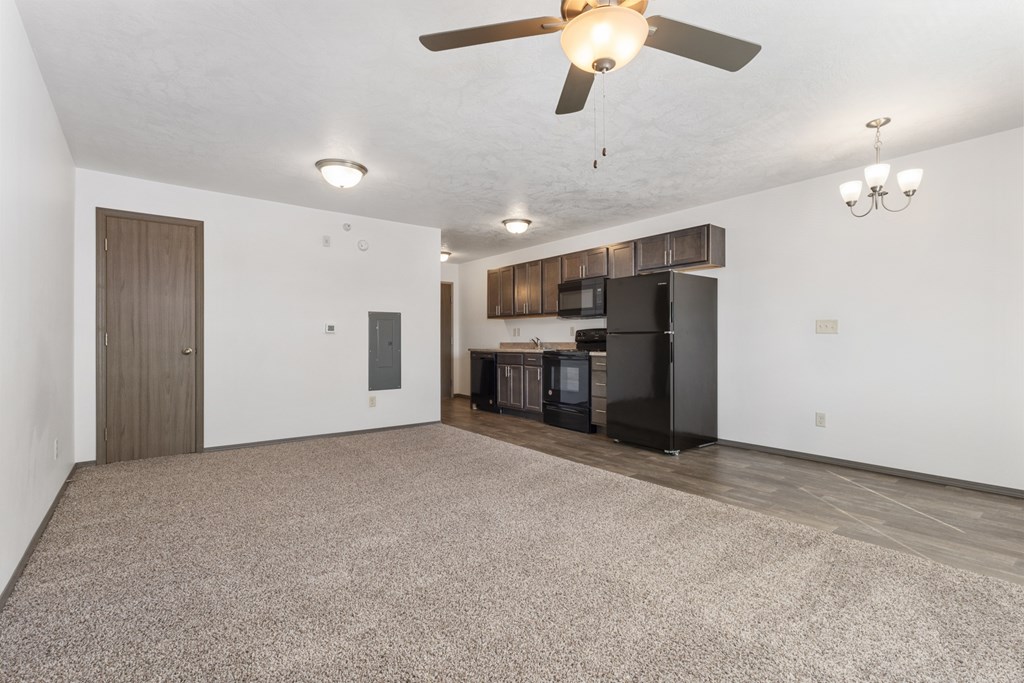 A spacious living room with a ceiling fan and a kitchen area in the background.