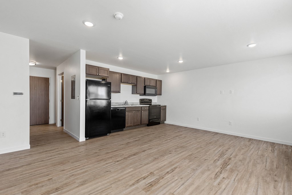 the living room and kitchen of an apartment with wood flooring and black appliances