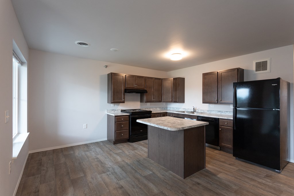an empty kitchen with a large island and black refrigerator
