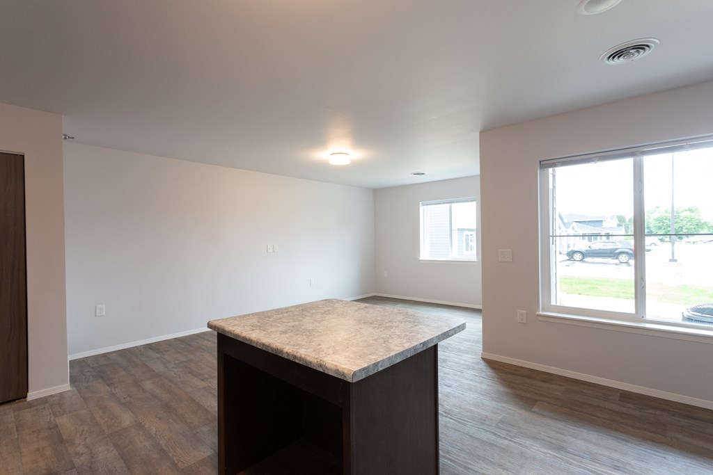 an empty living room with a large window and a kitchen island