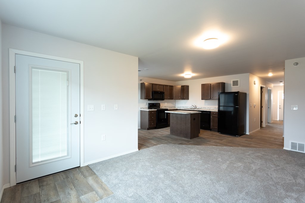 an empty living room and kitchen with a door open to a room with a kitchen