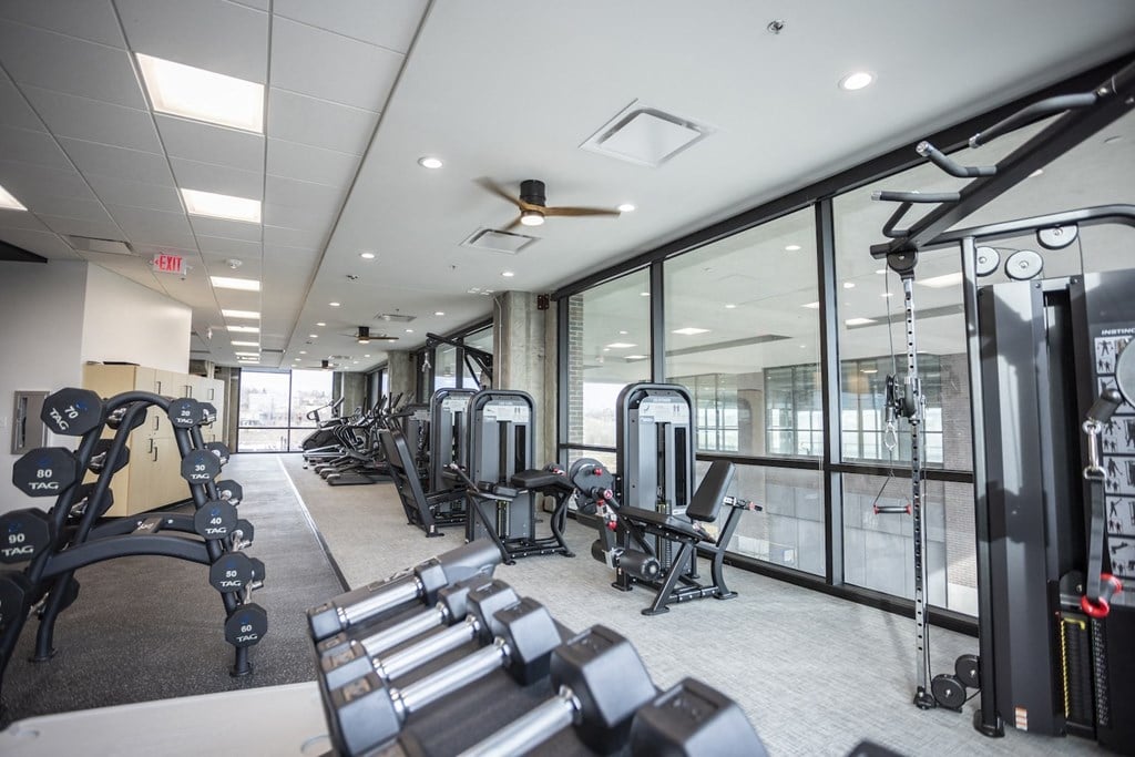 a gym with weights and cardio equipment on the floor and large windows