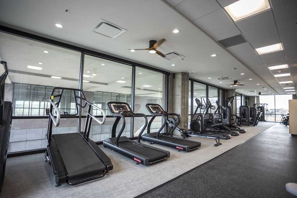 a gym with lots of cardio equipment on the floor and large windows